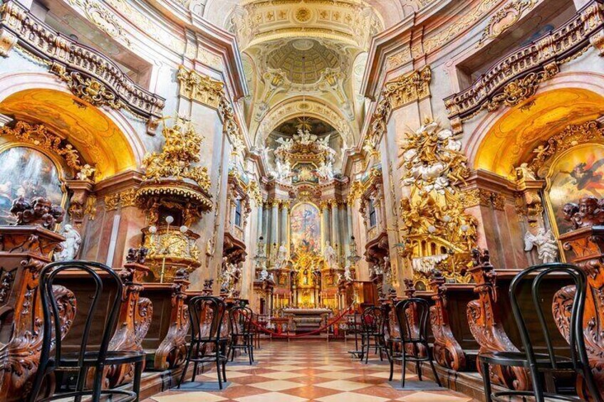 An ornate church interior with golden decorations, a checkered floor, and rows of chairs. 1