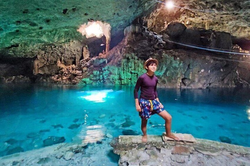 A person standing on a rock in a cave with clear blue water. 3