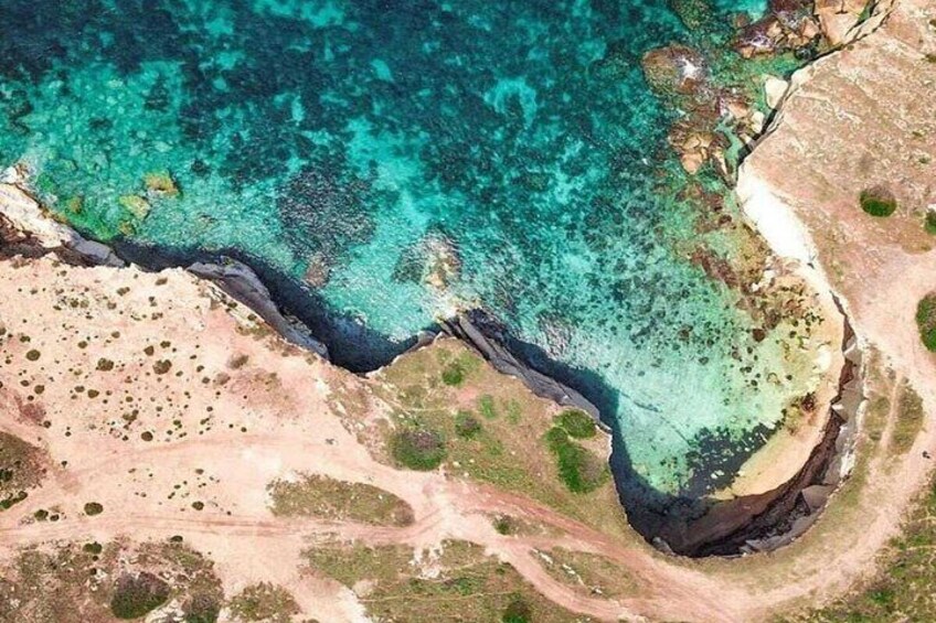 Un paysage côtier caractérisé par une eau turquoise et limpide, des affleurements rocheux et un sentier de terre qui mène à la plage. 5