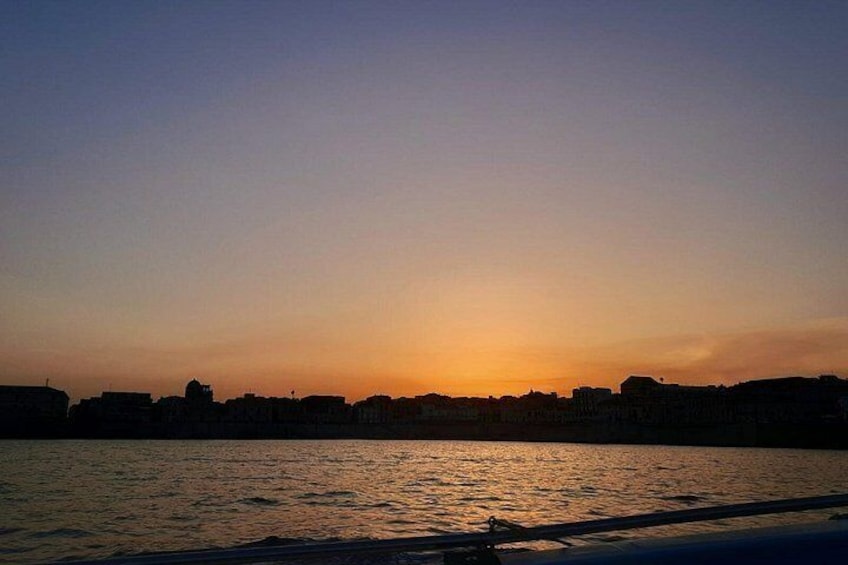 Un coucher de soleil sur une étendue d’eau, avec les silhouettes de bâtiments en arrière-plan. 4