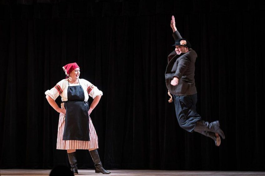 Two people in traditional costumes, one standing and one jumping. 2
