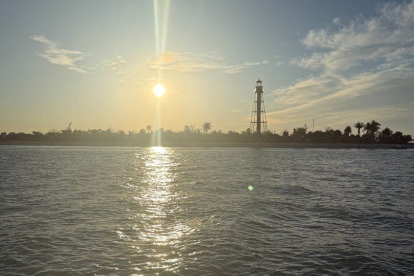 Un atardecer sobre una superficie de agua tranquila con un faro en la distancia. 3