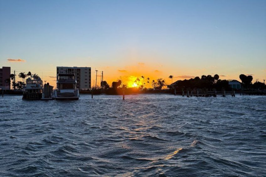 Un atardecer sobre un cuerpo de agua con barcos, edificios y palmeras. 4