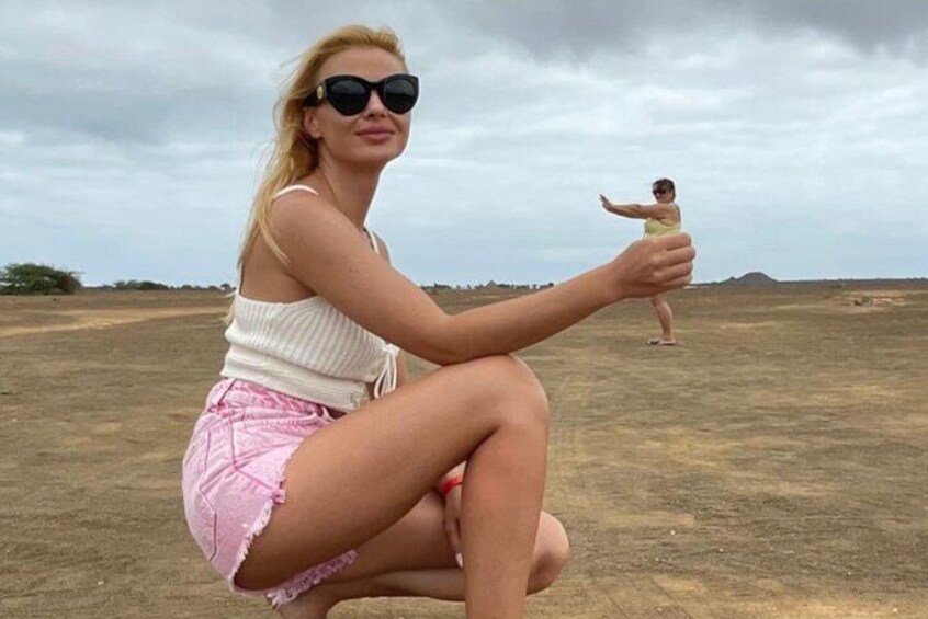 A person squatting on a dirt ground with a child standing in the background. 5