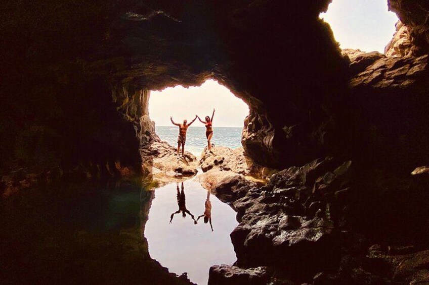 A cave entrance with a reflective water surface and two people standing at the opening. 5
