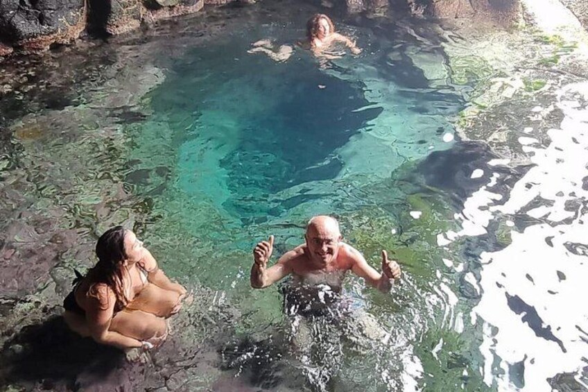 Eine Gruppe von Menschen in einem Naturschwimmbad mit klarem Wasser, umgeben von felsigem Gelände. 1