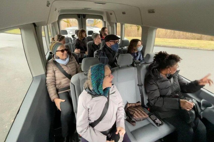 Interior de un vehículo con pasajeros sentados, algunos sosteniendo objetos, y una ventana que muestra una carretera. 2