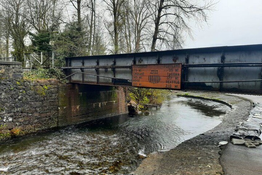 En smal vattenpassage under en bro, med en skylt som visar avstånden till Tacoma, Seattle och Spokane. 5