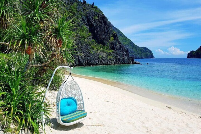 A beach with a hanging chair, clear turquoise water, and a rocky cliff. 5