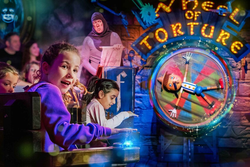 A ride with a robot character inside a colorful wheel, surrounded by a dark, themed environment with a sign reading "Wheel of Torture". 2