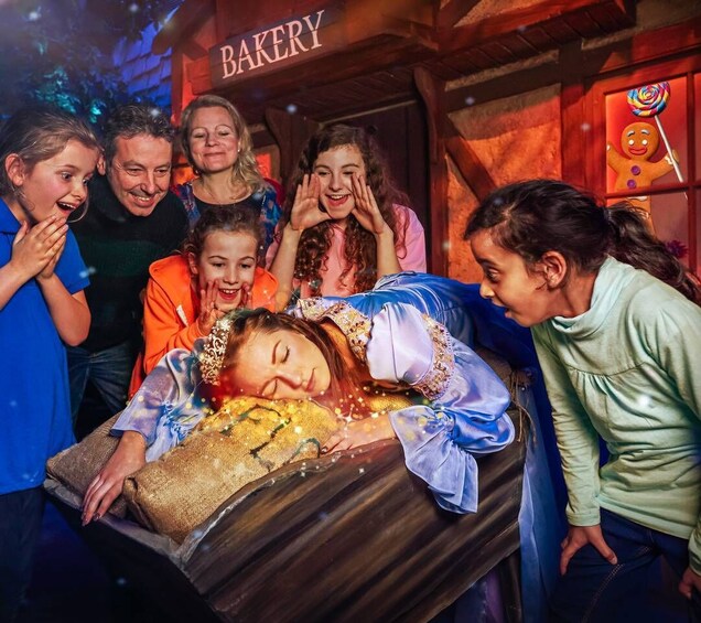 A group of people around a wooden coffin with a bakery sign in the background. 3