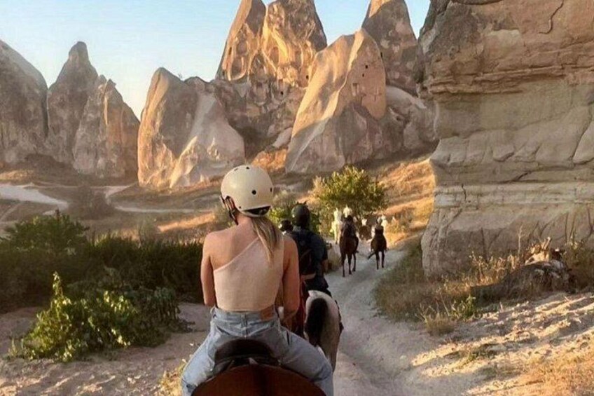 A person riding a horse on a dirt trail with rocky mountains in the background. 3