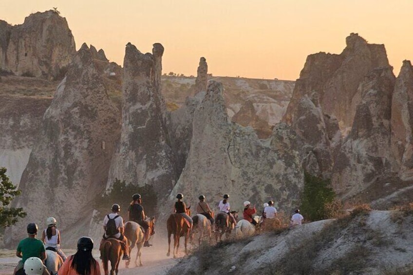 A group of people riding horses on a dirt trail with distinctive rock formations in the background. 1