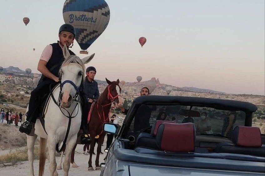 A person riding a white horse with a red saddle, a convertible car, and hot air balloons in the background. 4