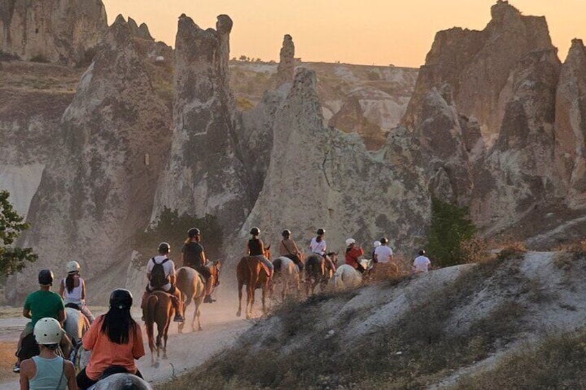 A group of people horseback riding on a trail with distinctive rock formations in the background. 2