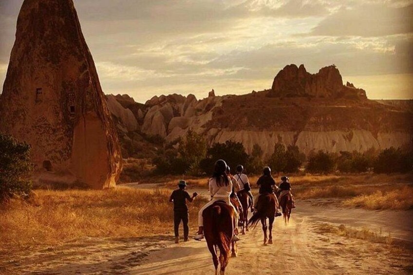 A group of people riding horses on a dirt road with a large rock formation in the background. 5