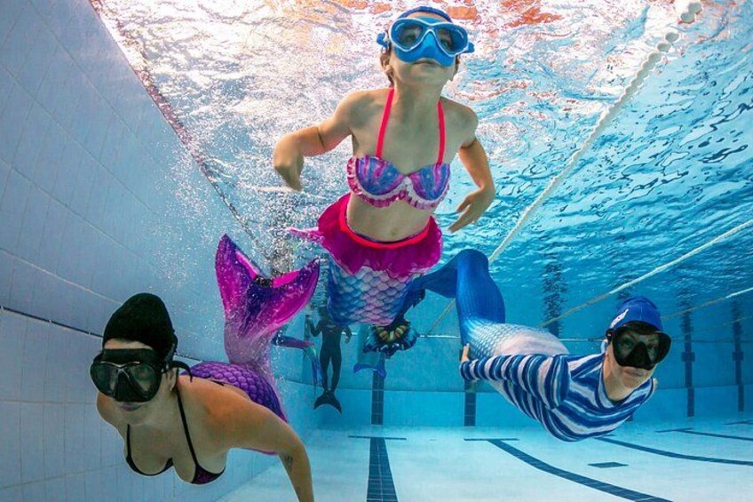 Escena submarina con tres personas en traje de baño y aletas, nadando en una piscina. 2