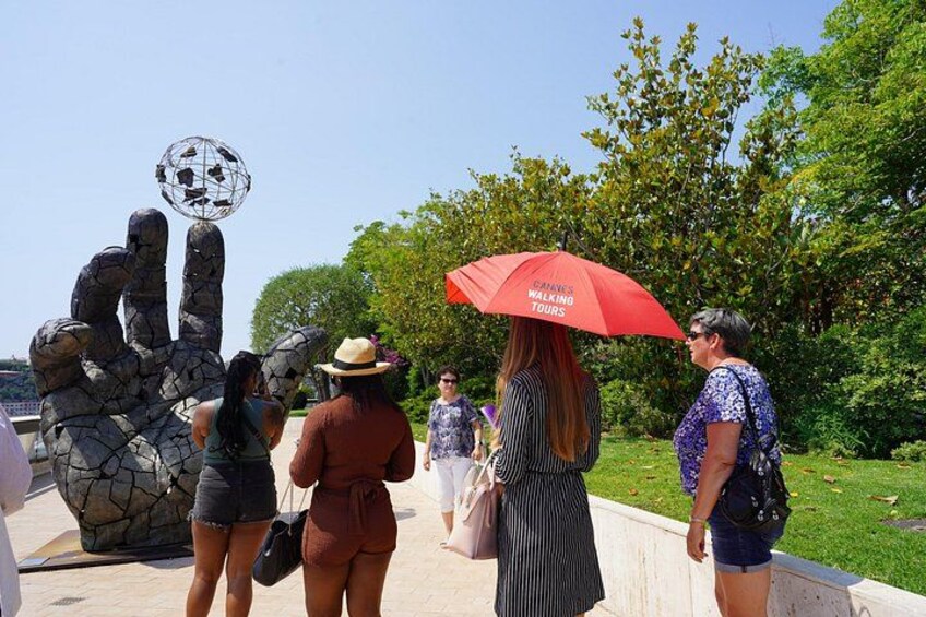 Un groupe de personnes se promène près d’une sculpture représentant une main tenant un ballon de football. 2