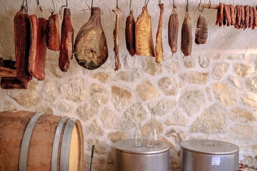 Diversos tipos de embutidos colgados en una pared, un barril de madera y dos recipientes metálicos. 1