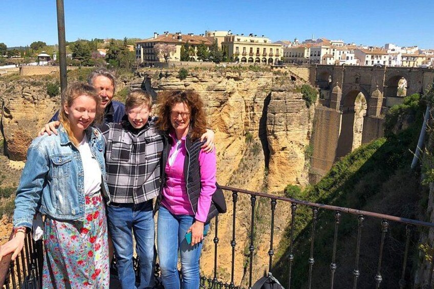 Un grupo de personas sobre un puente, con un acantilado rocoso y edificios al fondo. 2