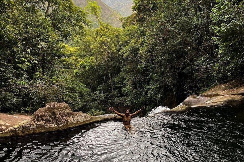 A person standing in a natural pool surrounded by lush greenery and rocky terrain. 1