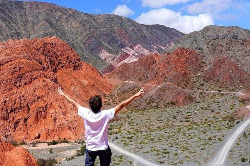 Une personne se tient debout, les bras tendus, dans un paysage montagneux caractérisé par des formations rocheuses rouges et une route. 4