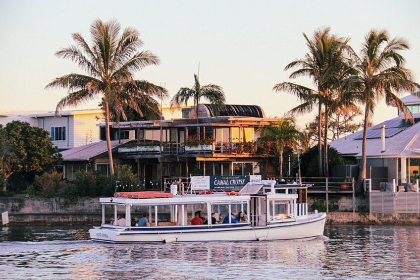 Ein Kanalrundfahrtschiff namens 'CANAL CRUISE' mit Passagieren, Palmen und Häusern entlang des Kanals. 1