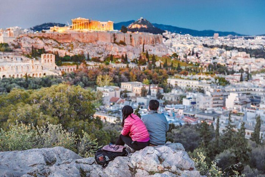 A couple sitting on a rocky outcrop overlooking a cityscape with ancient ruins and modern buildings. 5
