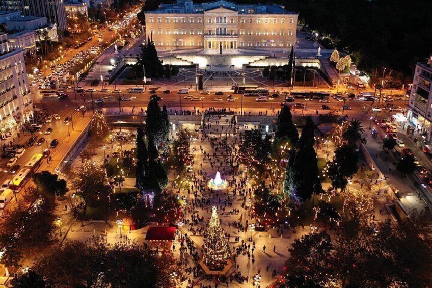 A city square at night with a large building in the background, trees, and a crowd of people. 3