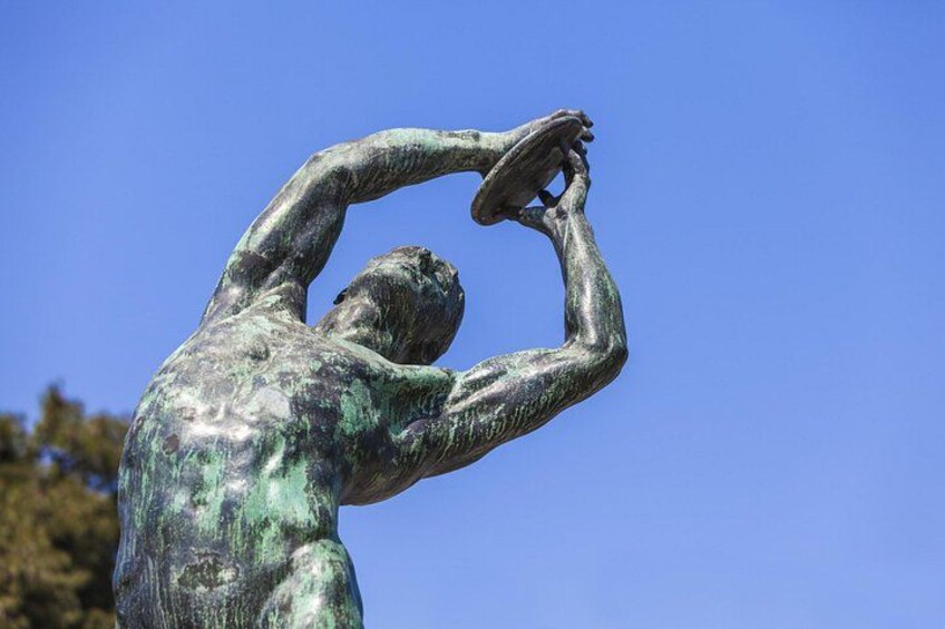 Una estatua de bronce de un hombre en una pose dinámica, sosteniendo un disco. 2