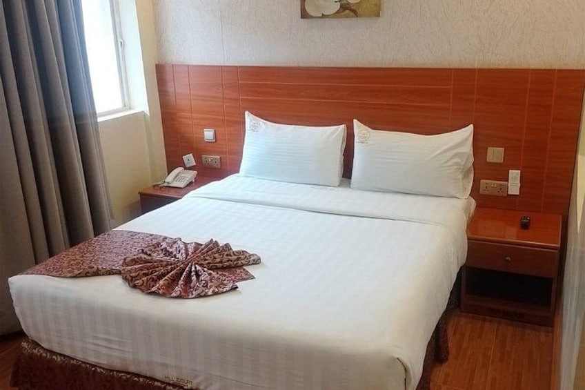 A hotel room with a large bed, wooden headboard, white bedding, and a decorative pillow arrangement. 3
