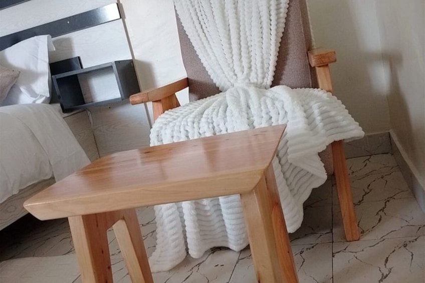 A wooden table and a chair with a white knitted blanket in a room with a tiled floor. 2