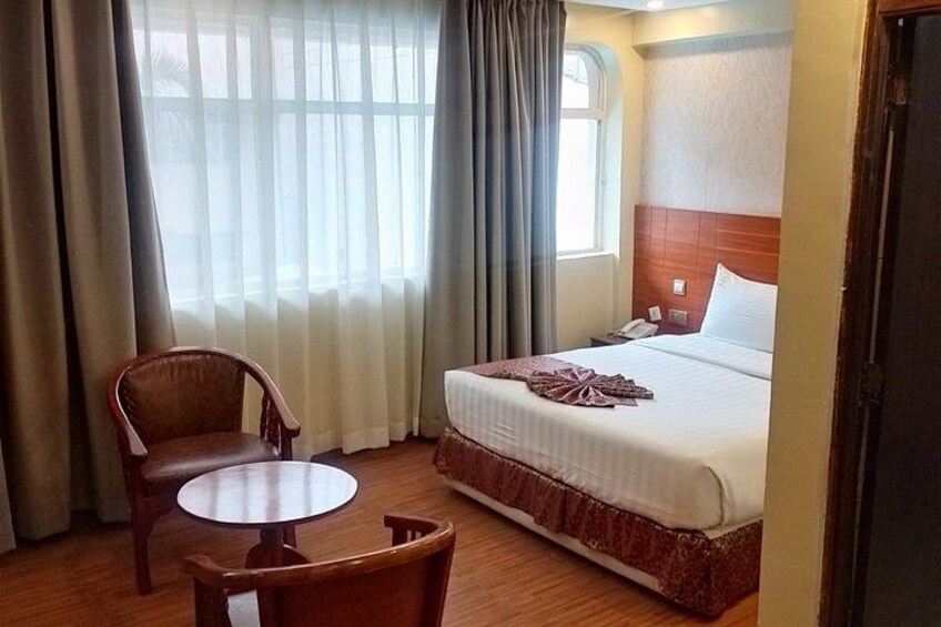 A hotel room with a bed, a chair, a small table, and a window with curtains. 4