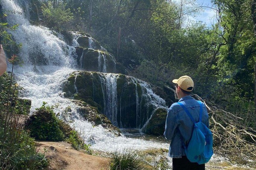 A waterfall in a forested area with a person observing it. 2