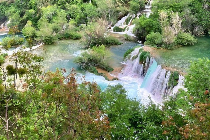 A waterfall cascading through a lush, green landscape with dense foliage and clear water. 1