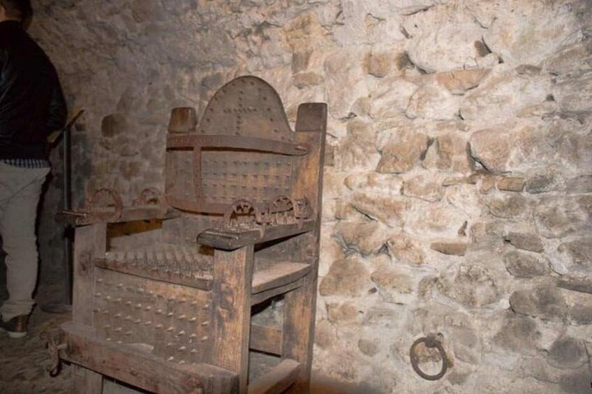 Ein alter, hölzerner Stuhl mit geschnitzter Lehne und Armlehnen, an einer Steinwand angelehnt. 3