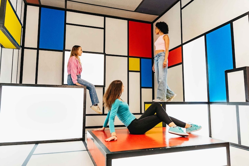 Tres personas en un espacio interior con paredes de diseños geométricos y coloridos. 1