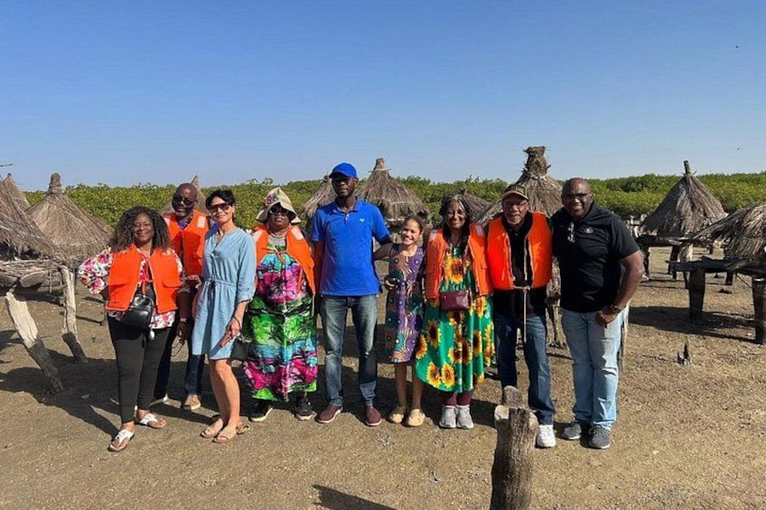 Un grupo de personas de pie al aire libre con construcciones de techo de paja al fondo. 4