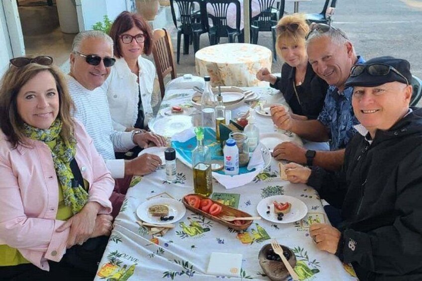 Eine Gruppe von Menschen speist an einem Tisch im Freien, mit Tellern voller Essen, Flaschen und einer Torte. 2