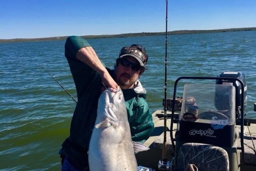 A person holding a large fish on a boat with calm water and a clear sky in the background. 2