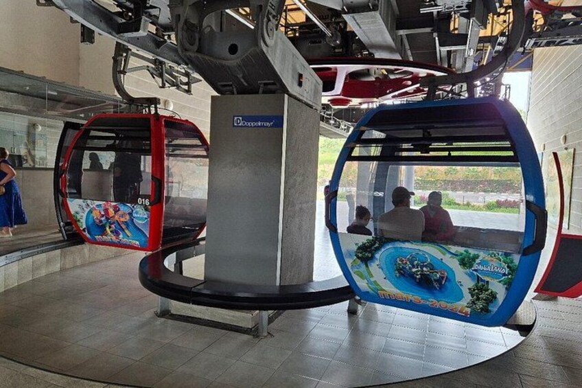 Een kabelbaan met twee gondels, waarvan er één rood en de andere blauw is, beide met kleurrijke motieven. 2