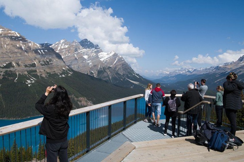 Un grupo de personas en una pasarela de madera con vistas a un paisaje montañoso y un lago. 2