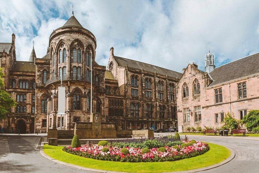 A historic building with a central dome and arched windows, surrounded by a well-maintained garden with pink flowers. 1