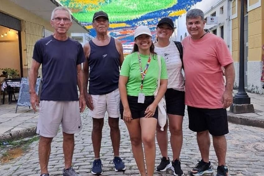 Un grupo de personas de pie en una calle adoquinada, con edificios y un mural colorido al fondo. 5