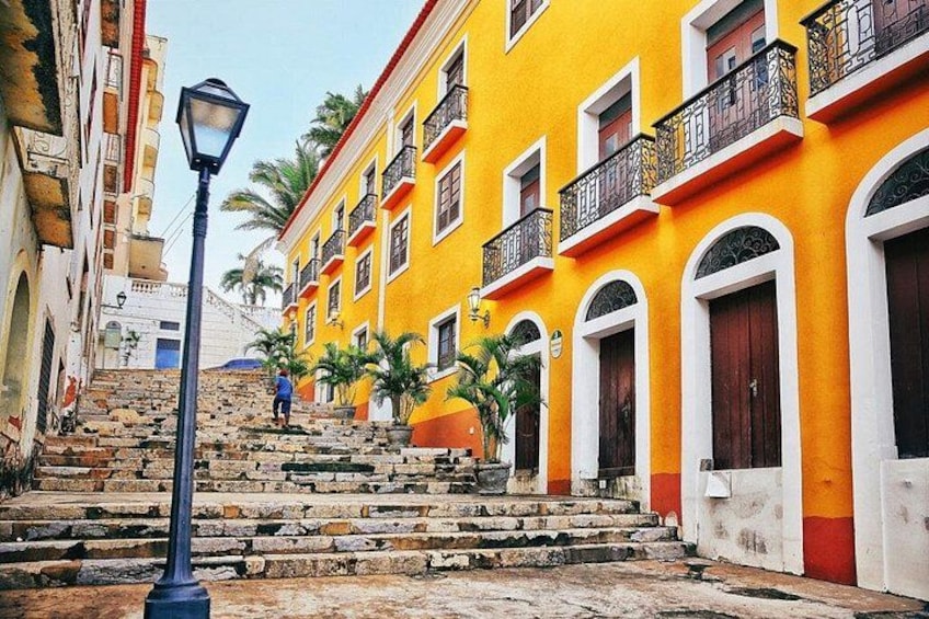 Una calle con edificios amarillos, una farola y palmeras. 1