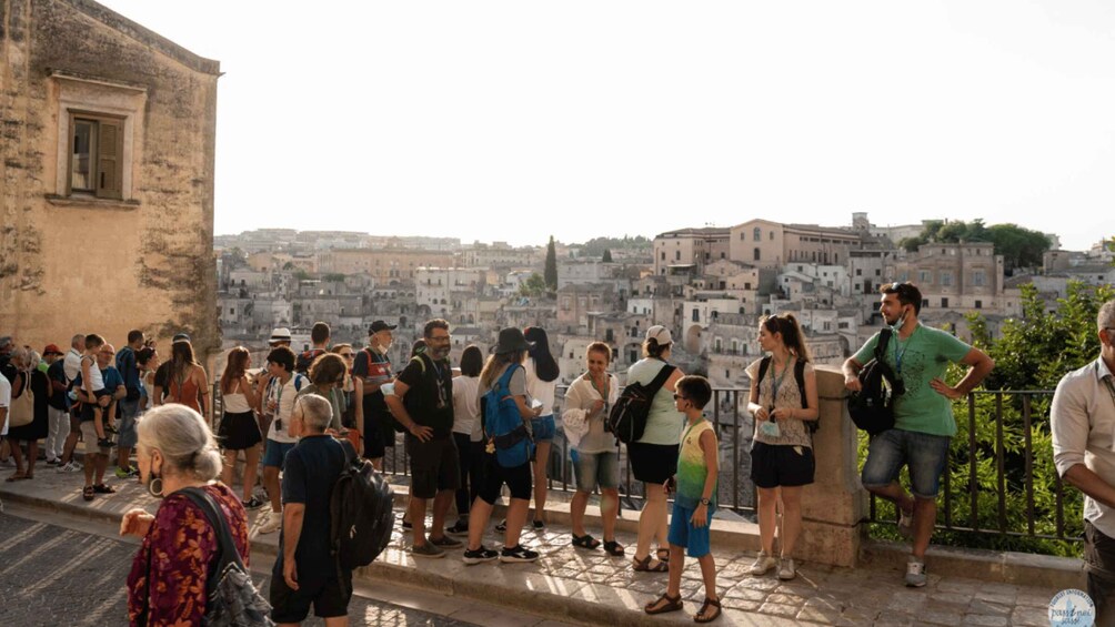 A group of tourists on a stone-paved walkway overlooking a densely packed cityscape with historic buildings. 1