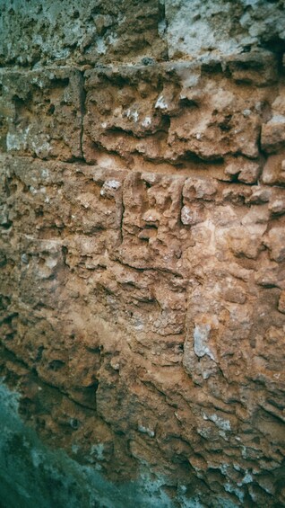 A textured stone wall with visible erosion and patches of discoloration. 3