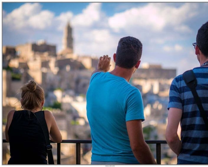 Three people overlooking a cityscape with historical buildings and a prominent tower. 1