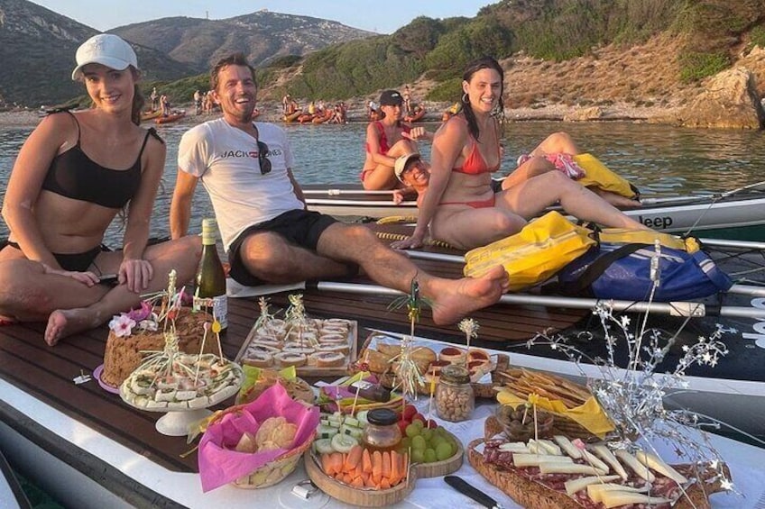 Personer på en båt som har dukat upp en picknick med bröd, frukt och dryck. 4
