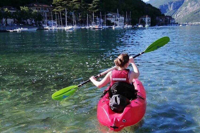 A person kayaking on a lake with clear water, surrounded by buildings and mountains in the background. 3